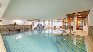 Una piscina interior con techo curvo, tobogán y zona de estar con sillas y mesas.