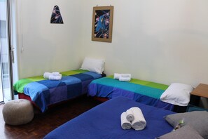 A room with two single beds, each with a blue and green striped bedspread, white pillows, and rolled towels. There is a small round ottoman and a framed picture on the wall. - Stendhal14 (Naples)