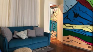 Una sala de estar moderna con un sofá azul, un taburete tejido y un cuadro abstracto colorido en la pared.