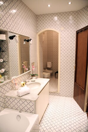 A bathroom with a large mirror, a bathtub, a sink, and a toilet visible through an archway. - Stendhal14 (Naples)