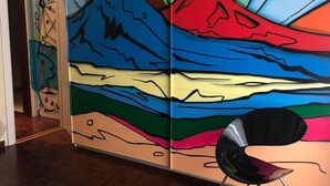 Una habitación con un cuadro abstracto y colorido en la pared, una silla negra moderna y suelo de madera.