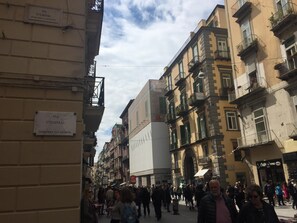 A busy street with people walking, buildings with balconies, and signs indicating 'VIA STENDHAL' and 'QUARTIERE SAN GIUSEPPE'. - Stendhal14 (Naples)
