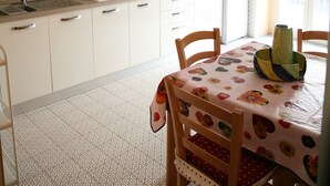 Una cocina con gabinetes blancos, una estufa a gas y un fregadero. Hay una mesa de comedor con sillas y un mantel estampado.