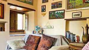 A cozy living room with a sofa, a small table with books, and various framed pictures on the walls.