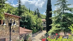 A stone building with a red-tiled roof, surrounded by lush greenery and tall trees.