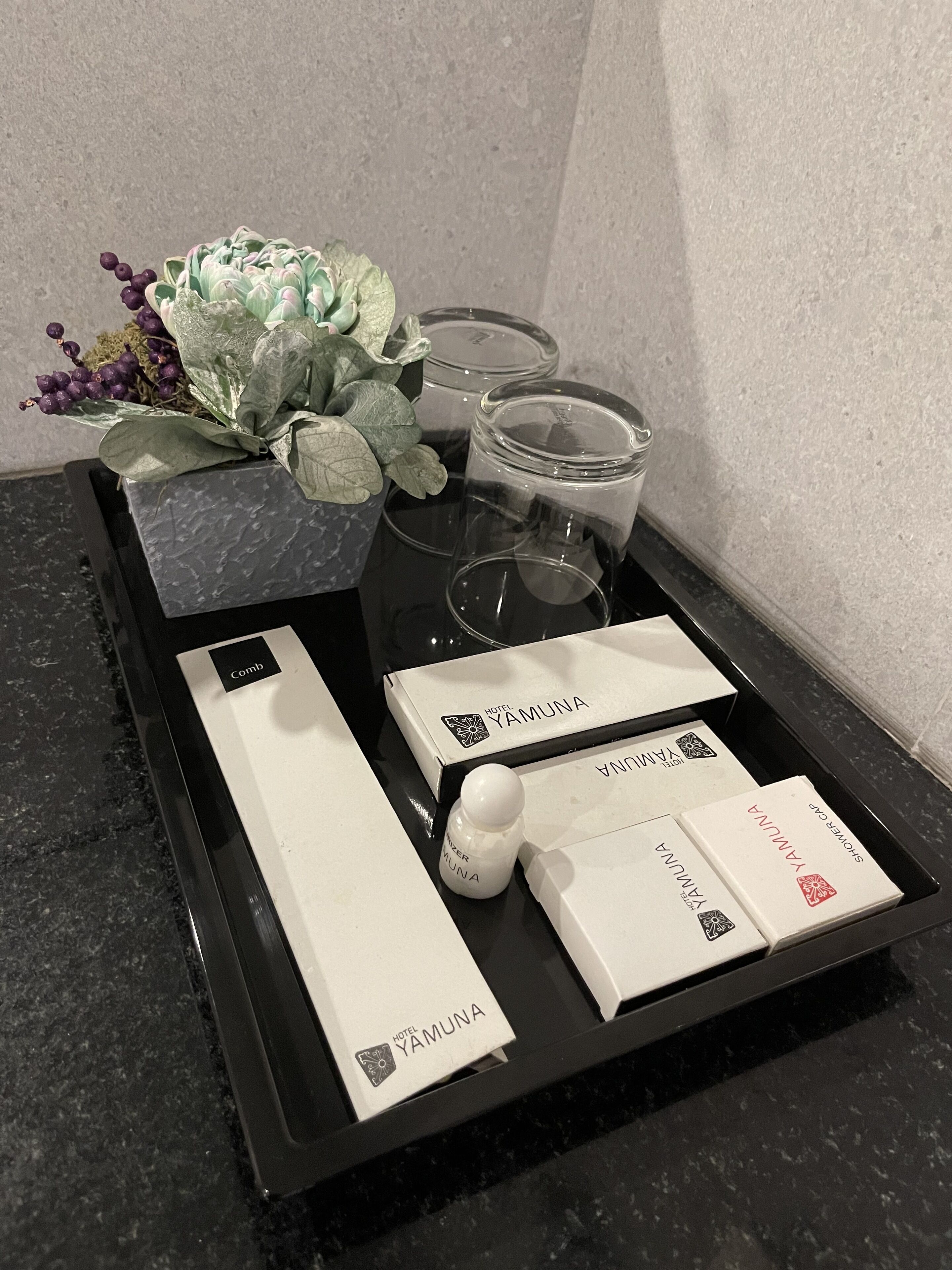 Ett bricka med hotellartiklar, inklusive en kam, en flaska och förpackningar märkta med texten ”YAMUNA”.