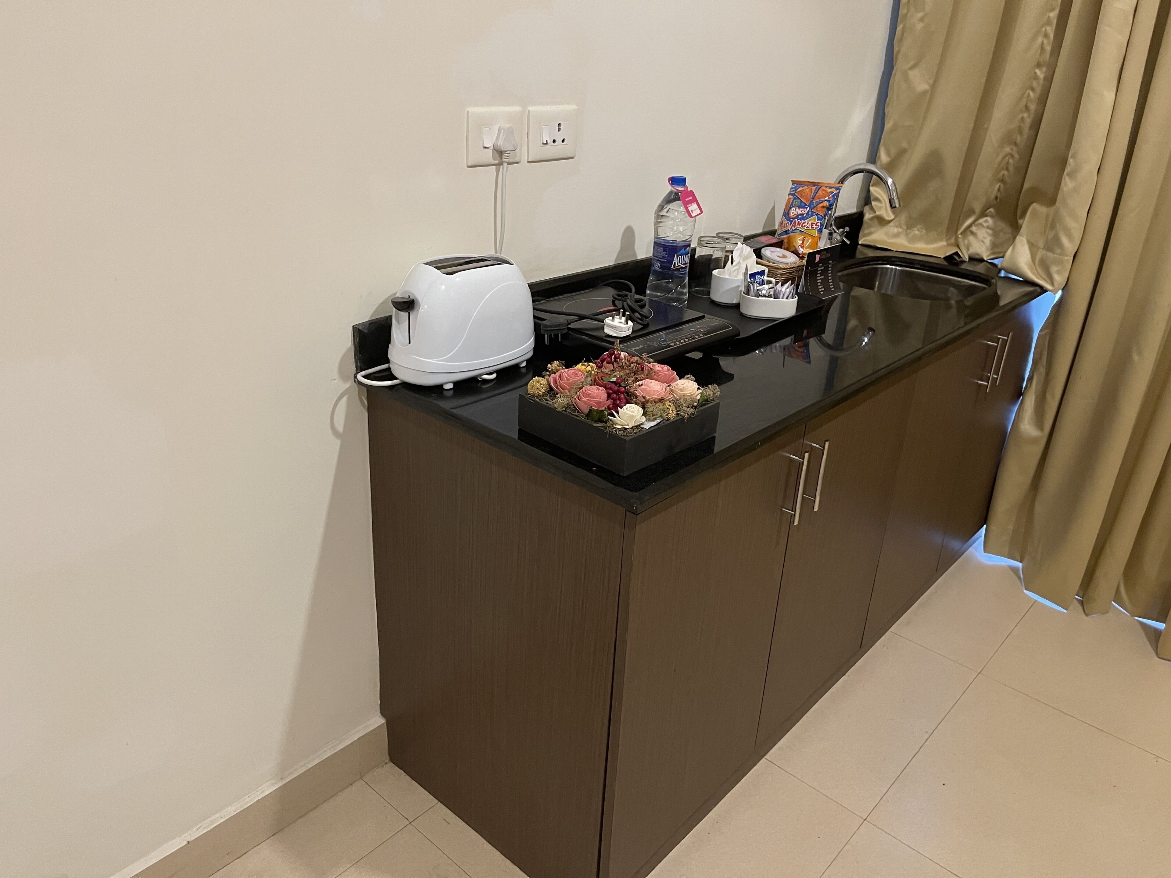 Una cucina compatta con un tostapane, una bottiglia d'acqua, un pacchetto di snack e un piccolo bouquet di fiori sul bancone.