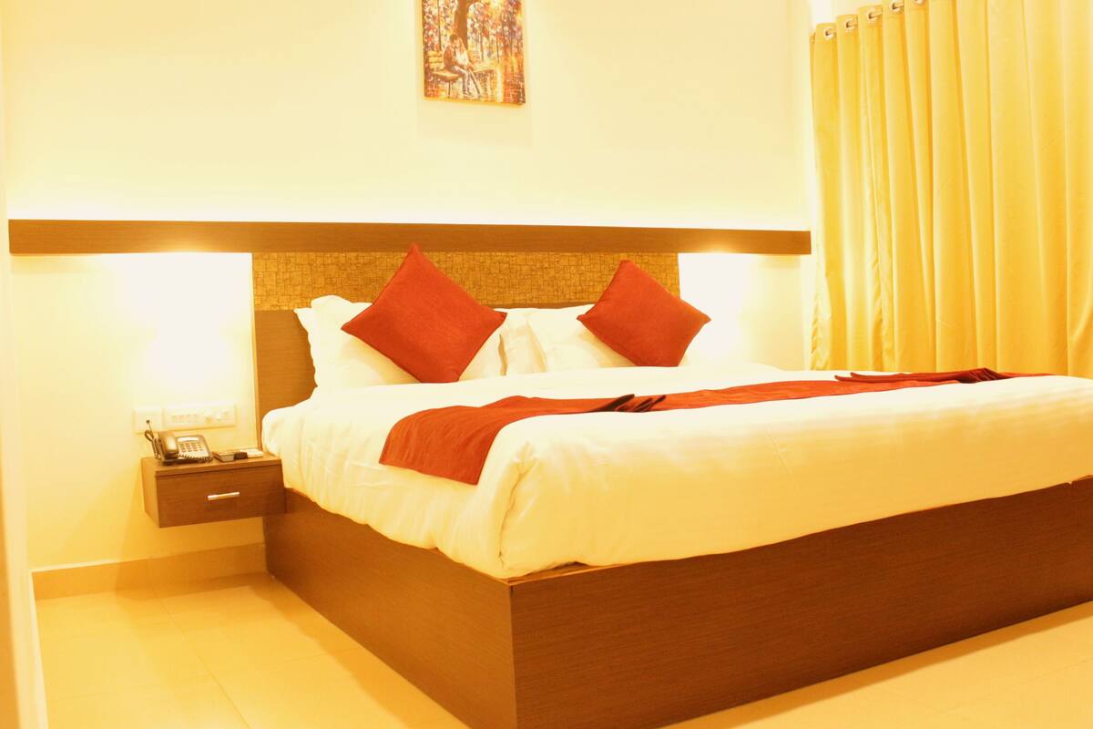 A hotel room with a large bed, a bedside table with a phone, and a painting on the wall.