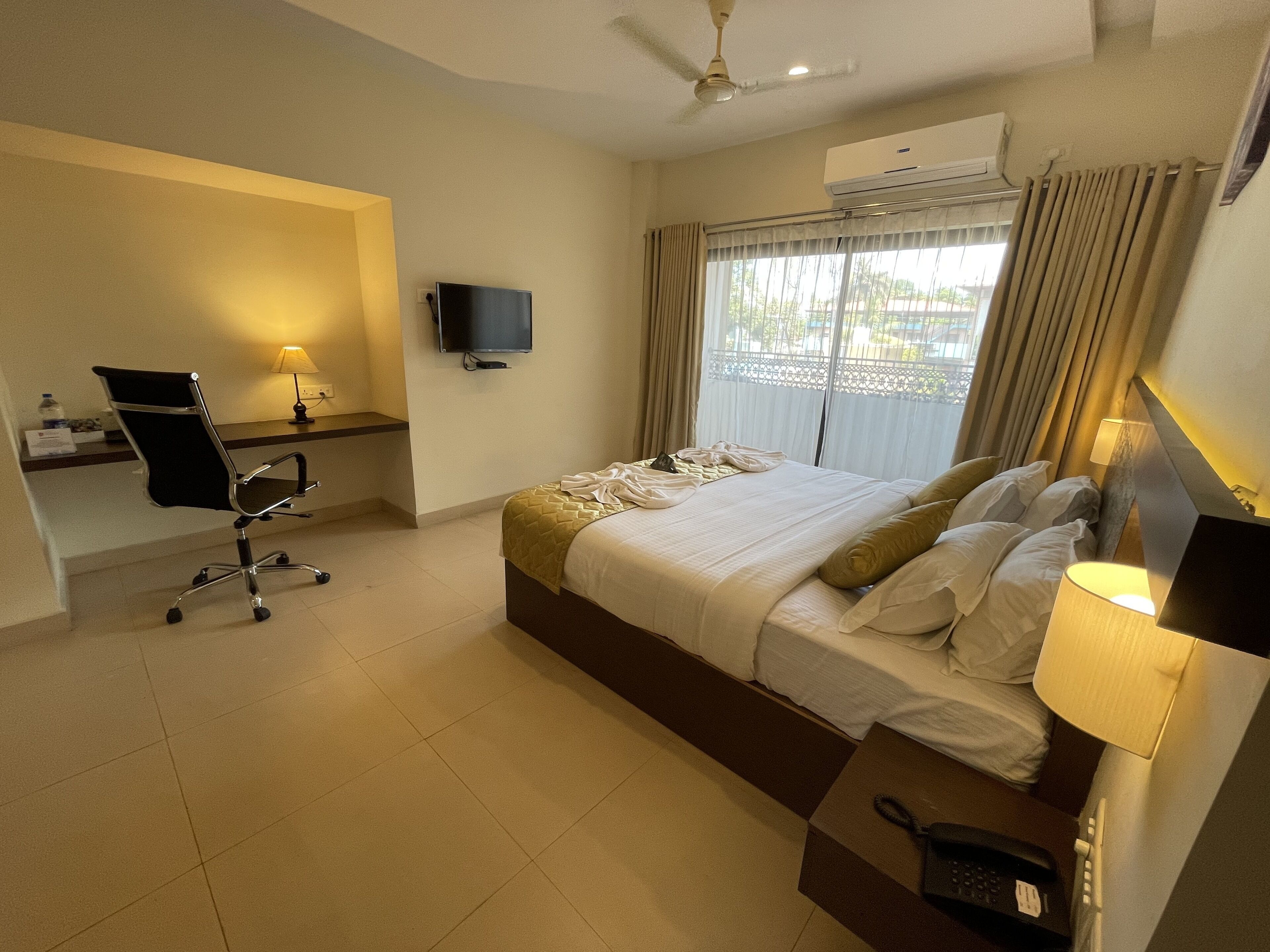 A hotel room with a bed, a desk with a chair, a television, and an air conditioning unit.