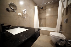 A modern bathroom with a black marble sink, a toilet, a shower with a glass door, and a hairdryer mounted on the wall. - Hotel Yamuna (Adoor)