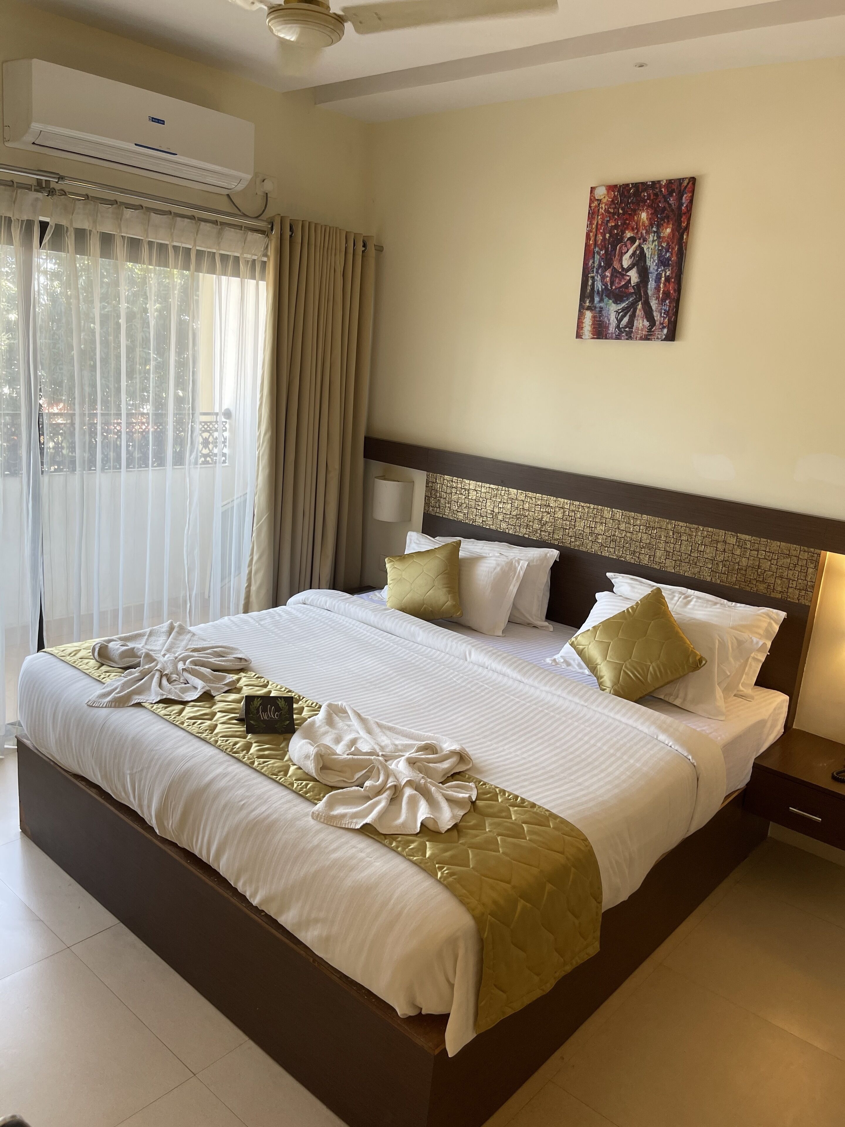 Habitación de hotel con una cama grande, una mesita de noche, un aire acondicionado, una ventana con cortinas y un cuadro en la pared.
