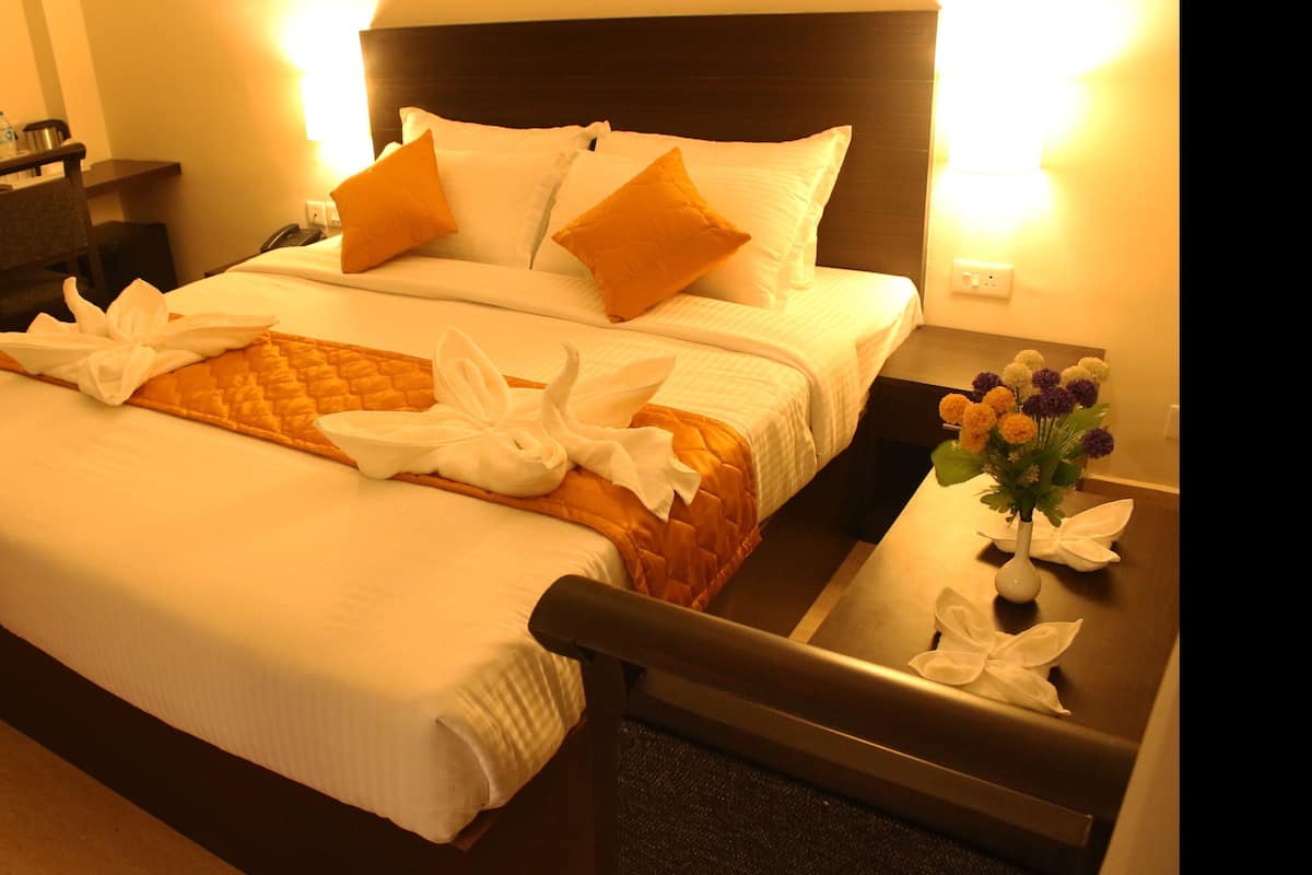 A hotel room with a bed, a nightstand, a chair, and a vase with flowers.