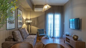 A modern living room with a sofa, a dining table, and a TV mounted on the wall. - Finesse Luxury Flat (Athens)