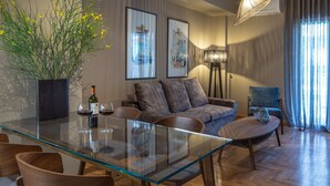 A modern living room with a glass dining table, a sofa, and a chair. There is a potted plant, a wine bottle, and two glasses on the table. - Finesse Luxury Flat (Athens)