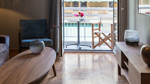 A modern living room with a sofa, a round table, and a chair. A vase with flowers is on the table. - Finesse Luxury Flat (Athens)