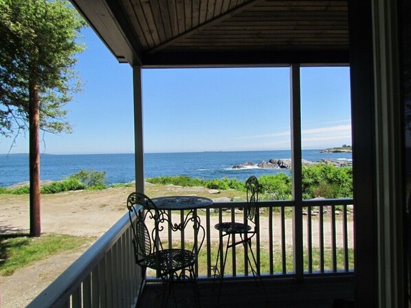A covered outdoor area with a view of the sea, featuring a small table and chairs.