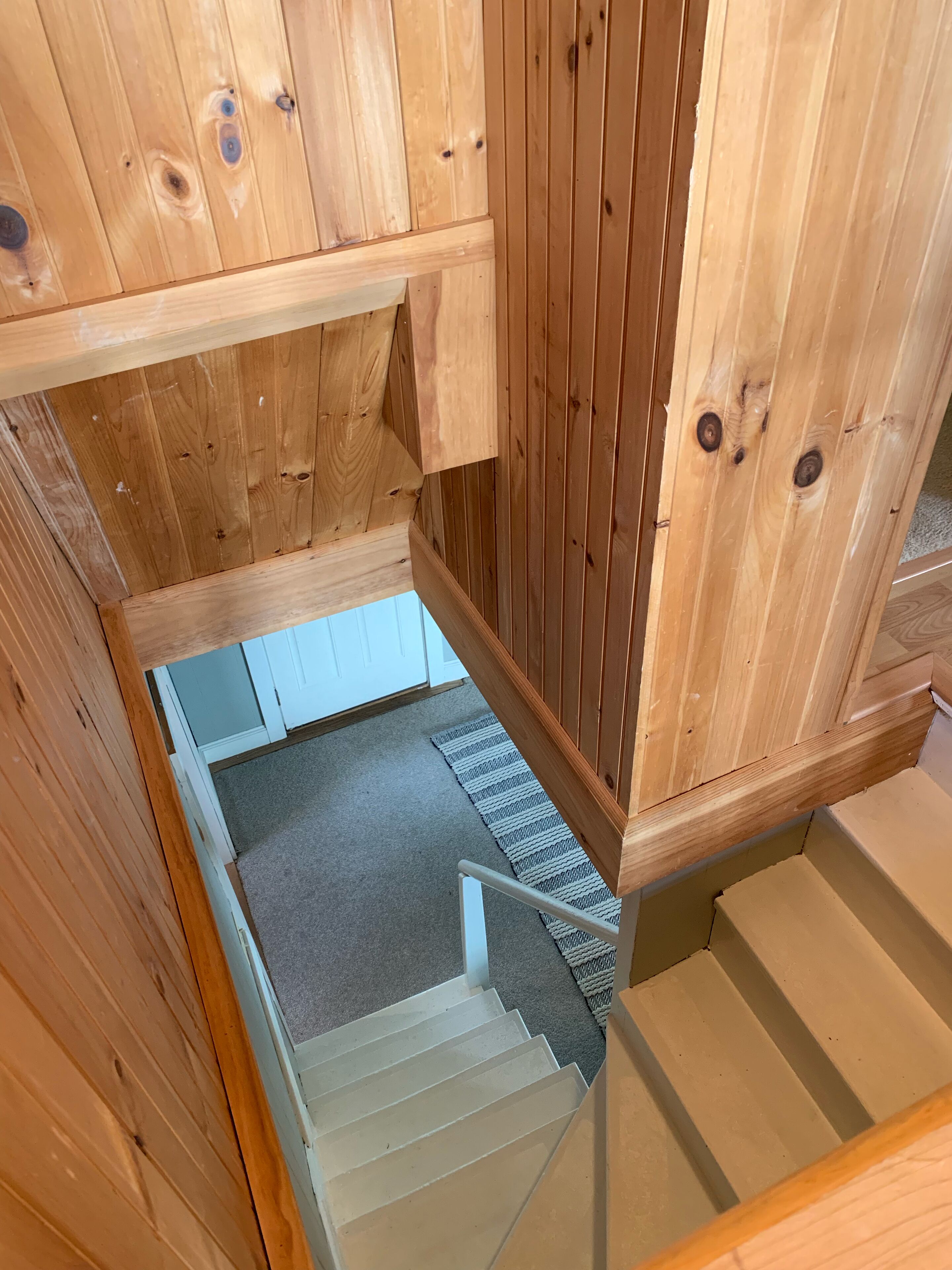 A wooden staircase with a carpeted landing area and a white door at the top.