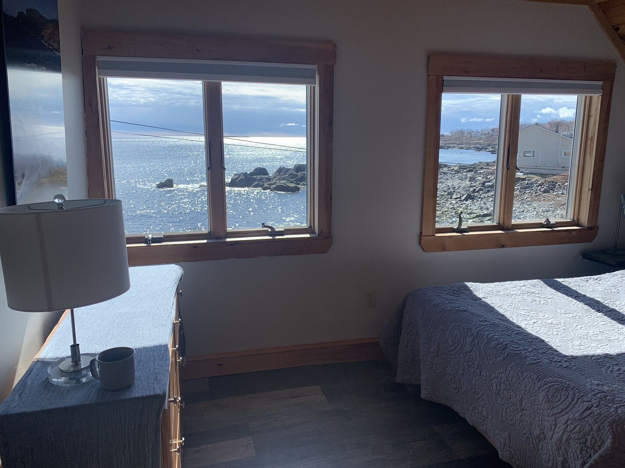 A bedroom with two windows overlooking a rocky coastline.