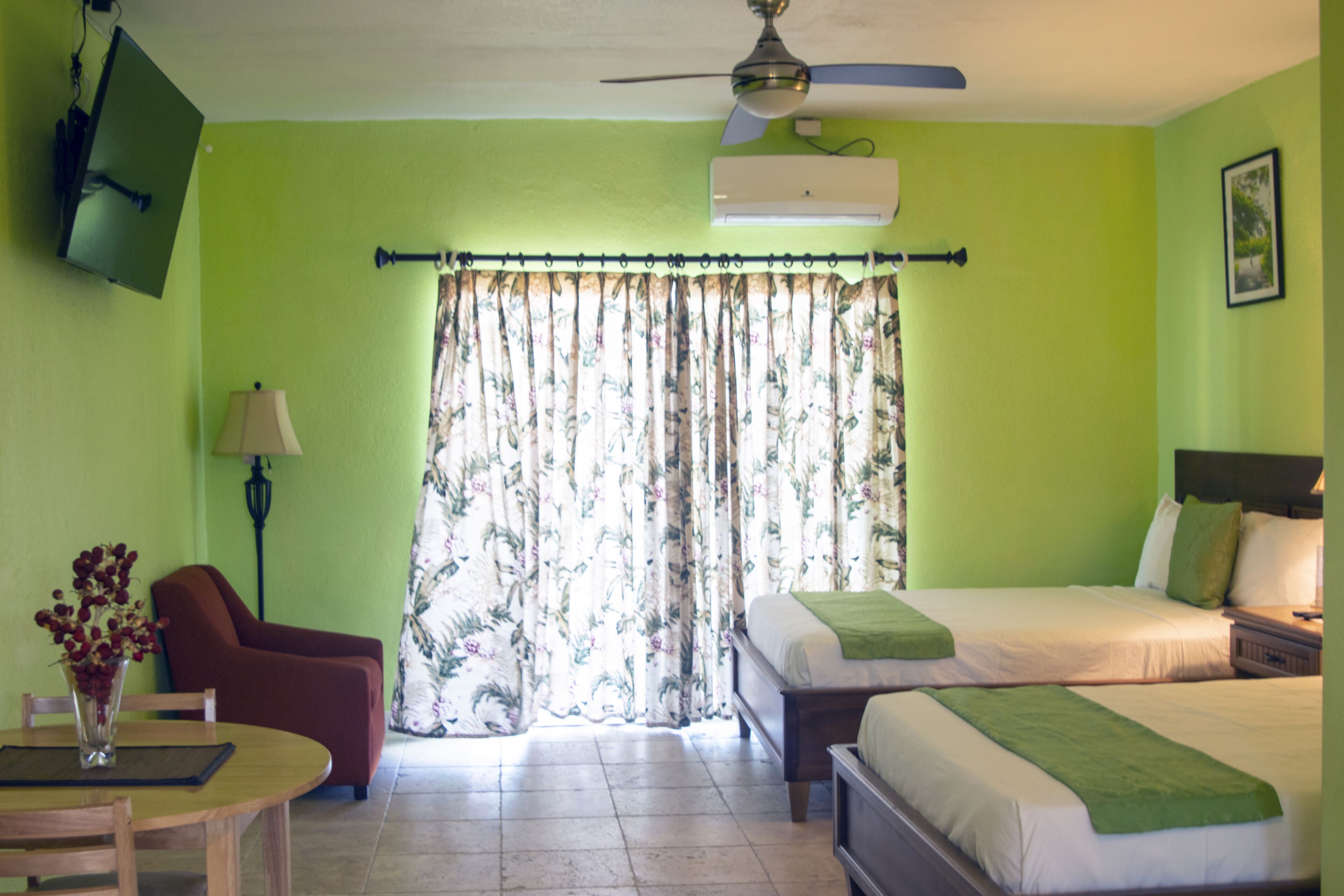 Ein Hotelzimmer mit einem Bett, einem Sessel, einem Tisch mit Blumenvase und einem Deckenventilator.