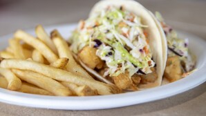 Um prato com dois tacos de peixe e batatas fritas.