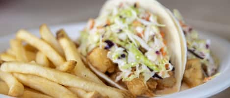 A plate with two fish tacos and a side of French fries.