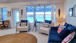 A living room with wicker furniture, a blue sofa, and a view of the sea through large windows.