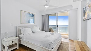 Een slaapkamer met een bed, nachtkastje en uitzicht op de oceaan door een schuifdeur.