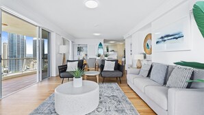 Een moderne woonkamer met een grijze bank, een ronde salontafel en een uitzicht op de stad door grote ramen.