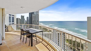 Een balkon met een tafel en stoelen, met uitzicht op een strand en de skyline van de stad.