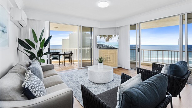 Een moderne woonkamer met een grijze bank, een ronde salontafel en uitzicht op de oceaan door grote glazen schuifdeuren.