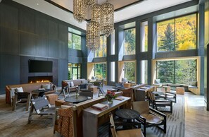 A spacious indoor area with multiple seating arrangements, a fireplace, and large windows offering views of autumn foliage.