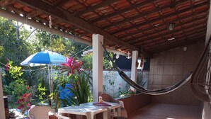 Une terrasse extérieure avec un sol carrelé, une table avec des chaises, un hamac et des plantes en pot.