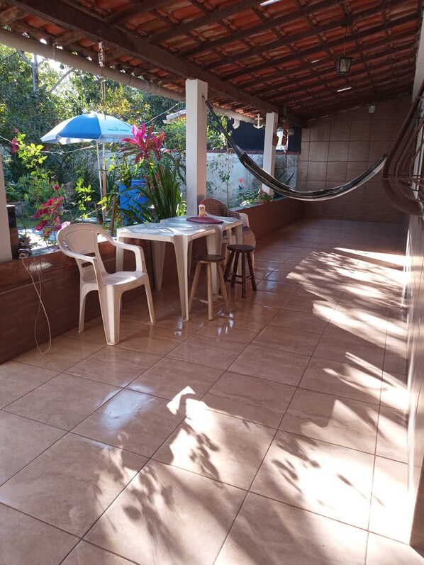 An outdoor patio with a tiled floor, a table with chairs, a hammock, and potted plants.