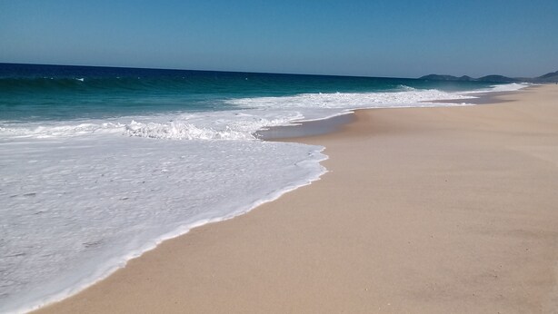 Une vaste plage de sable fin, avec des vagues douces et un ciel bleu dégagé.