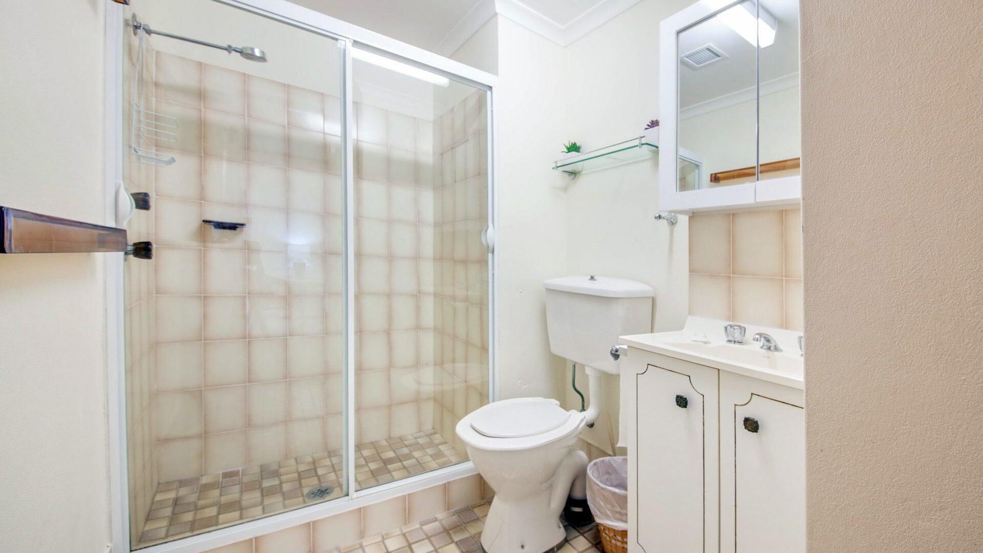Une salle de bain avec une douche à parois de verre, des toilettes et un lavabo avec un miroir au-dessus.