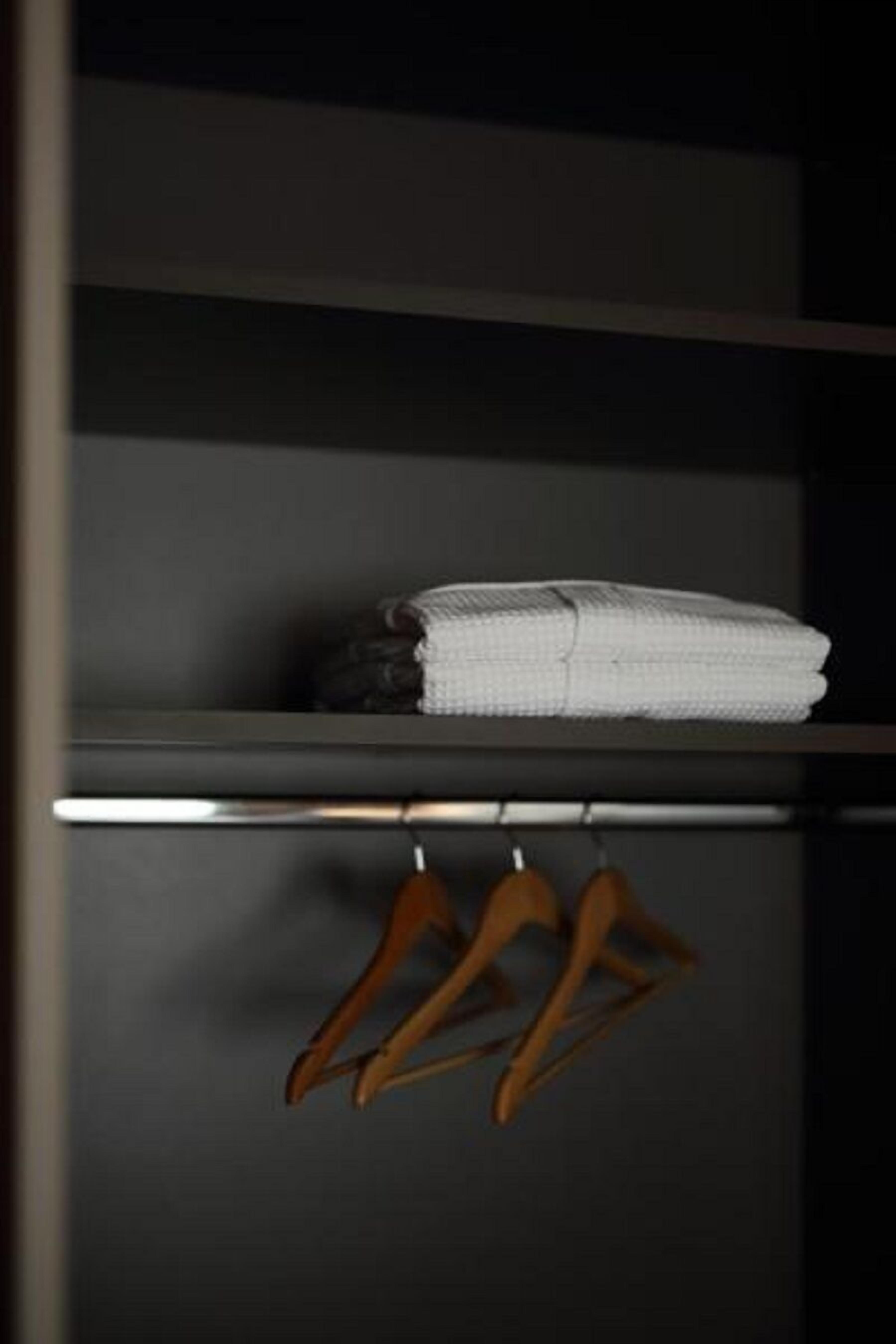 A closet with a folded white towel on a shelf and three wooden hangers below.