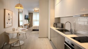 Una cocina moderna con microondas, lavabo y horno empotrado. Hay una zona de comedor con mesa y sillas, y una sala de estar con cama y televisor.