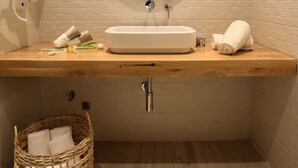 Un baño con tocador de madera, lavamanos blanco, espejo, perchero y cesta de mimbre.