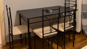 A dining area with a table and chairs, a TV mounted on a shelf, and a radiator. - Small & Cozy Flat near Hospitals (Zografos)