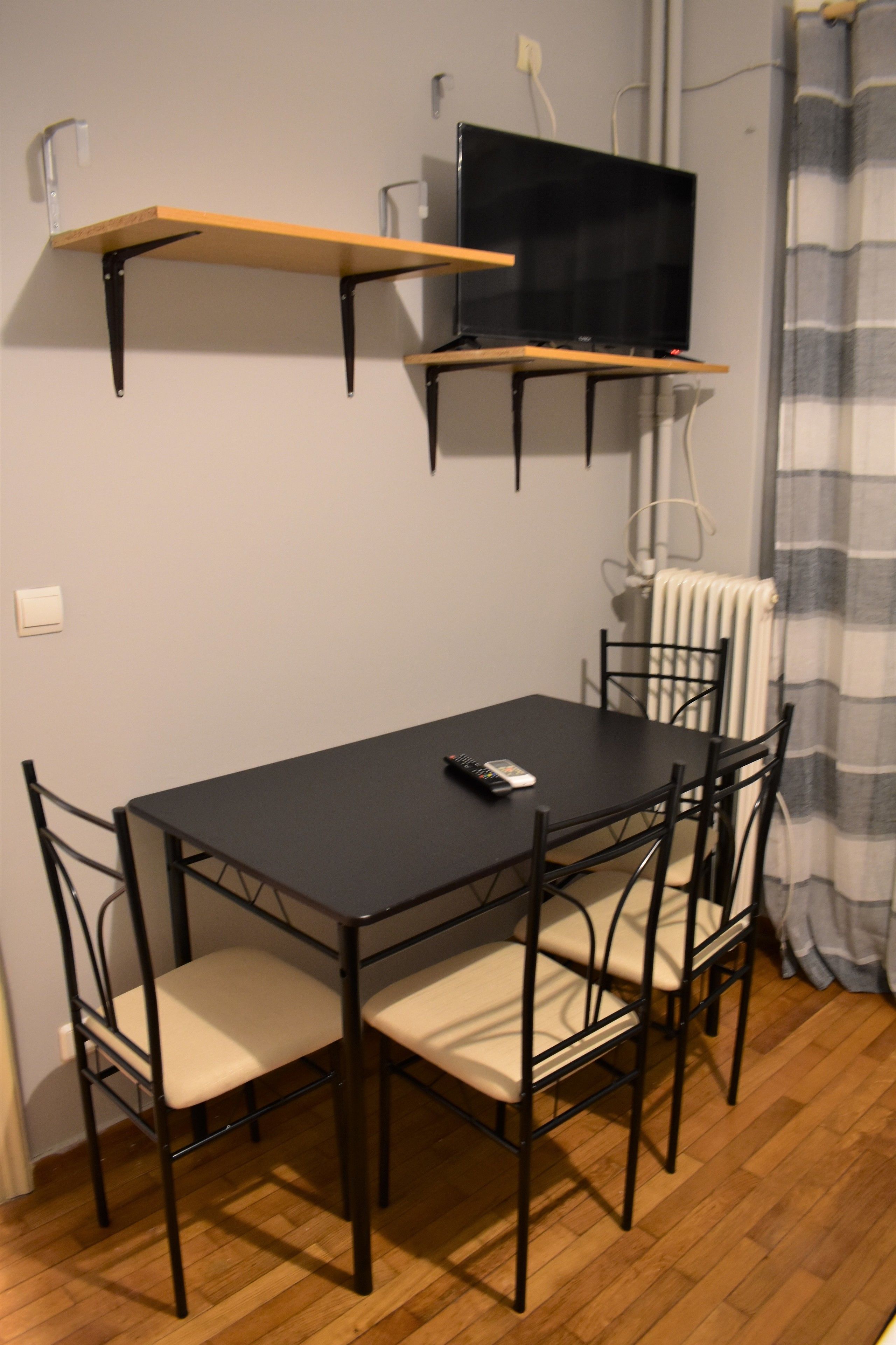A dining area with a table and chairs, a television mounted on the wall, and a radiator.
