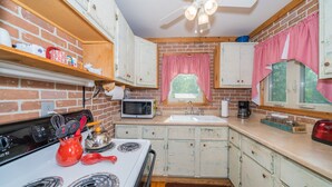 A kitchen with a brick wall, wooden cabinets, a stove, a microwave, and a window with red checkered curtains.