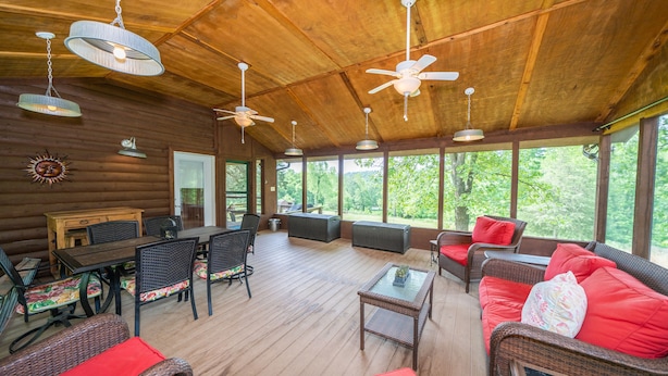 A covered outdoor area with wooden flooring, wicker furniture, and ceiling fans.