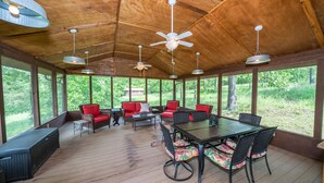 A covered outdoor area with wooden flooring, wicker furniture, and a glass table.