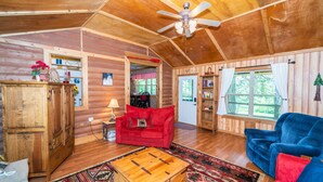 A cozy cabin interior with a wooden ceiling, a red sofa, a blue armchair, and a bookshelf.