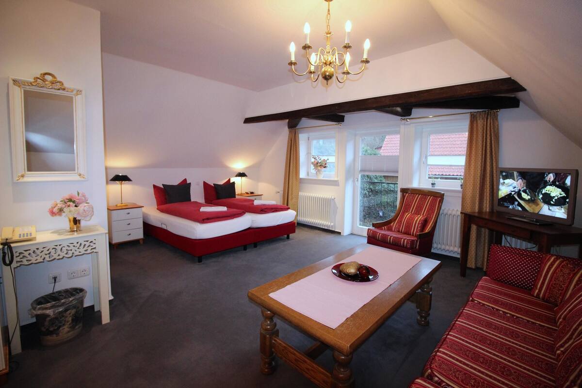 Una habitación acogedora con cama, una mesa de madera, un sofá rojo, televisor y candelabro.