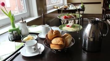 Un desayuno con una mesa preparada para dos, que incluye una bandeja con pasteles, una jarrón y una taza de café.