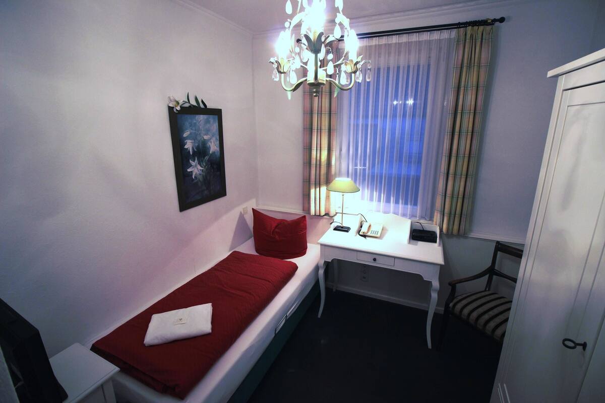Un dormitorio pequeño y ordenado con una cama individual, un escritorio, una silla y un armario.