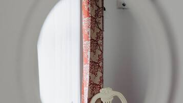 Una habitación con escritorio blanco, una silla, teléfono y un espejo que refleja una puerta con cortinas estampadas.