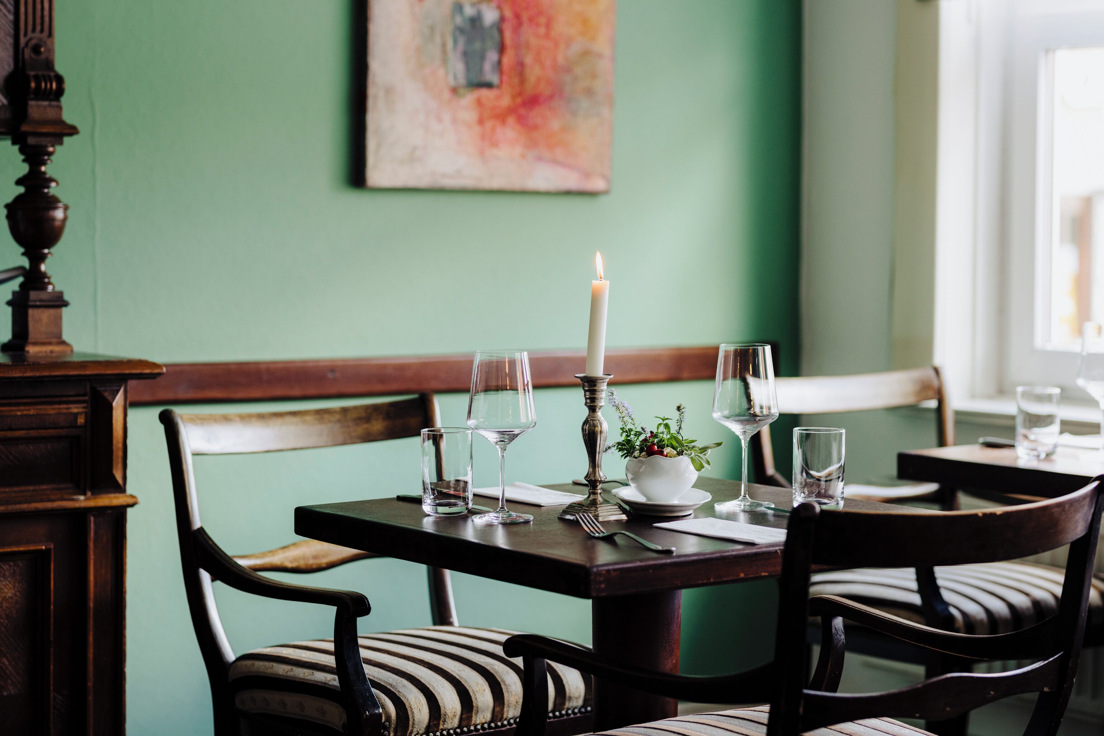 A dining table set with chairs, a candle, and a bowl of flowers.