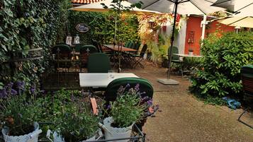 An outdoor patio area with a table and chairs, surrounded by potted plants and a brick wall.